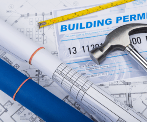 building plans and permits spread out on a table with a hammer on top.
