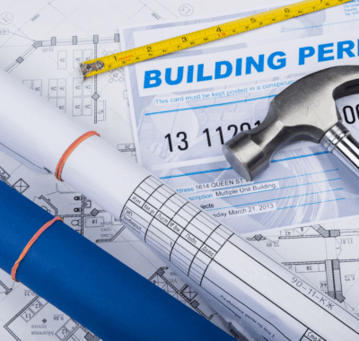 construction and planning building plans and permits spread out on a table with a hammer on top.
