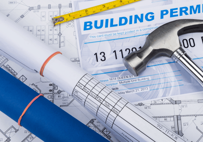 building plans and permits spread out on a table with a hammer on top.